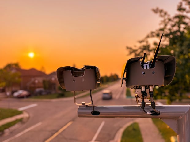 Two speed cameras mounted across a street with sunset in the background